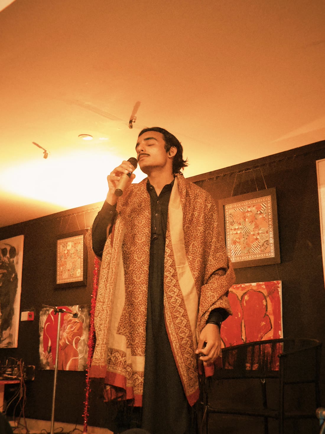 Random Mirza singing, draped in a traditional shawl under warm light